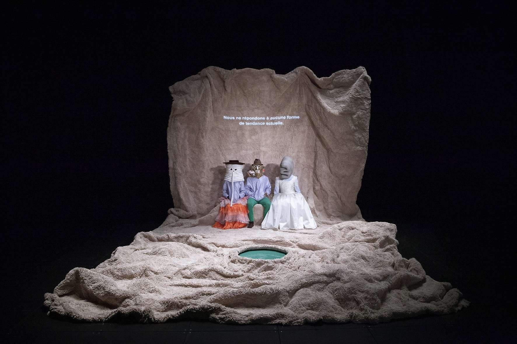 Trois personnages originaux sont assis dans un décor en moumoute avec un faux lac. Au fond est inscrit : Nous ne répondons à aucune tendance actuelle. 