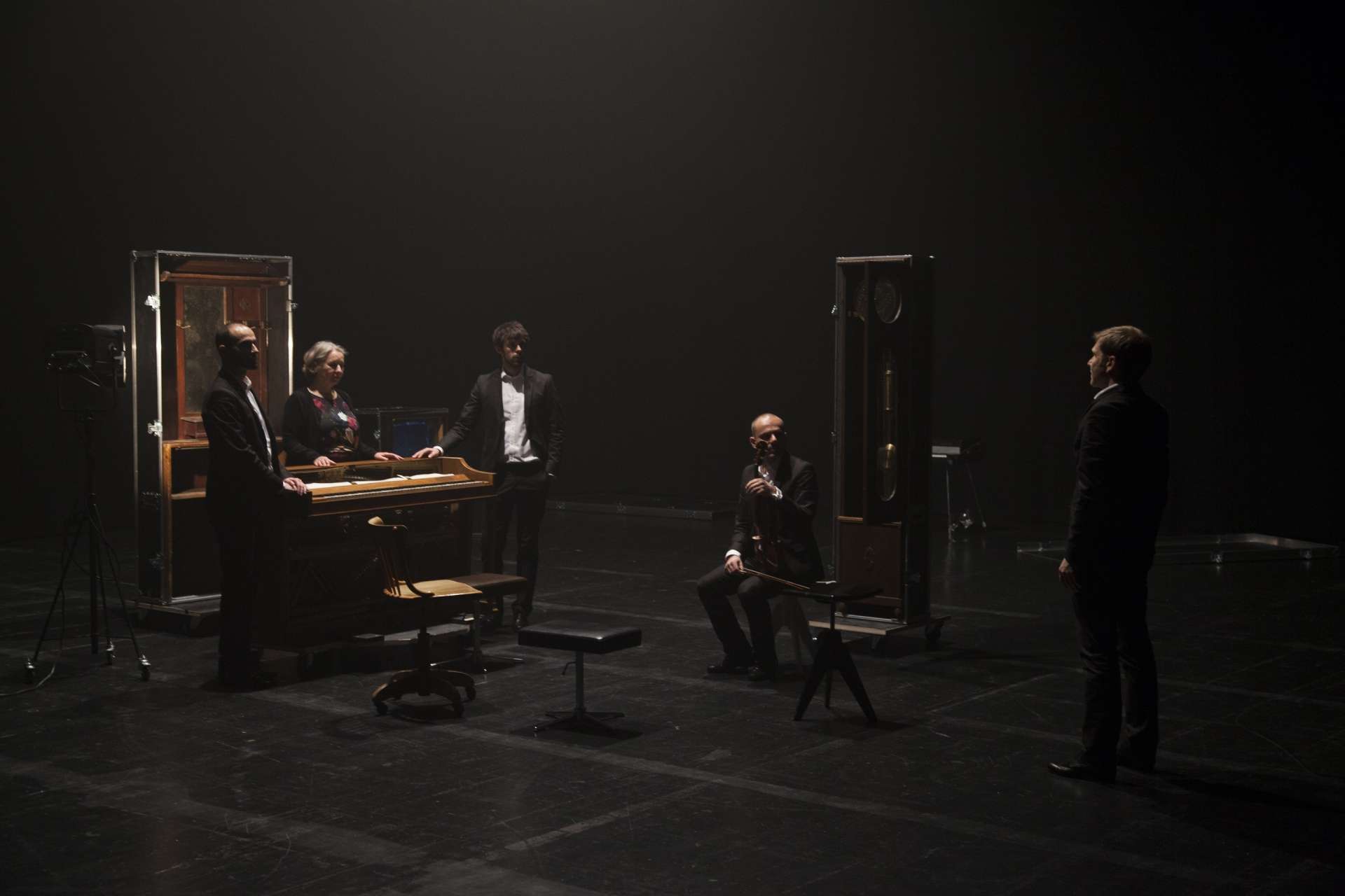 Dans la pénombre, quatre musiciens et une musicienne discutent autour d'un piano. 