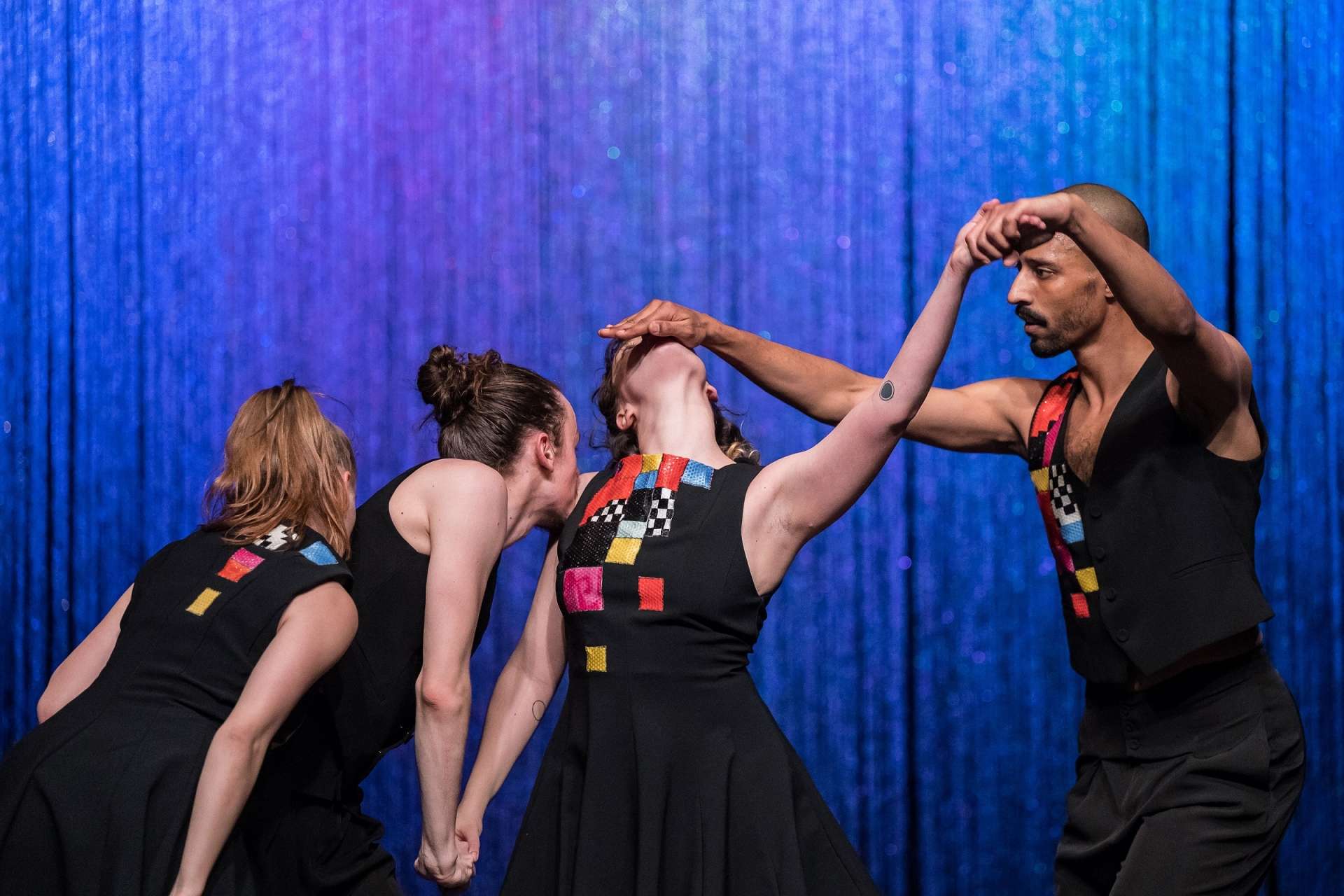 Photo de quatre danseurs (deux danseurs et deux danseuses). Une danseuse au milieu de l'image est le centre de l'attention. Un danseur à droite de l'image lui tient la main, le bras levé, tandis que de son autre main, il lui cache le visage, celui-ci étant penché en arrière. A gauche de l'image, un autre danseur lui tient la main, le long de son corps, tandis qu'il lui embrasse l'épaule. Enfin, la deuxième danseuse se tient derrière ce danseur et lui embrasse le dos. 