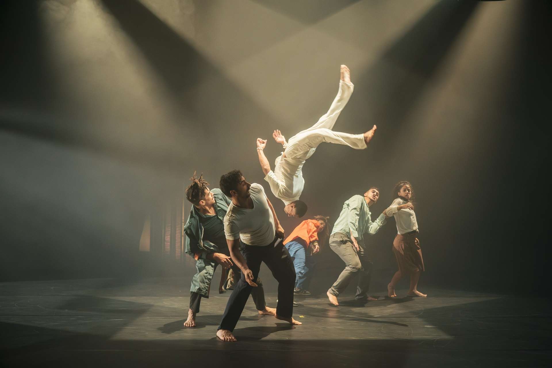 Photo du spectacle KA-IN, un groupe de danseuses et danseurs penché sur le côté, faisant de la place à un danseur faisant un salto au milieu de la scène.