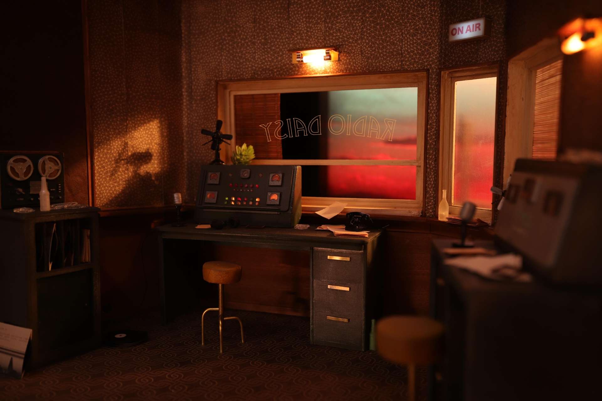 Une petite radio, avec des fenêtres et des équipements de radio, est montrée dans une représentation miniature d'un studio. Sur la fenêtre, légèrement surélevée, il est écrit "RADIO DAISY". 