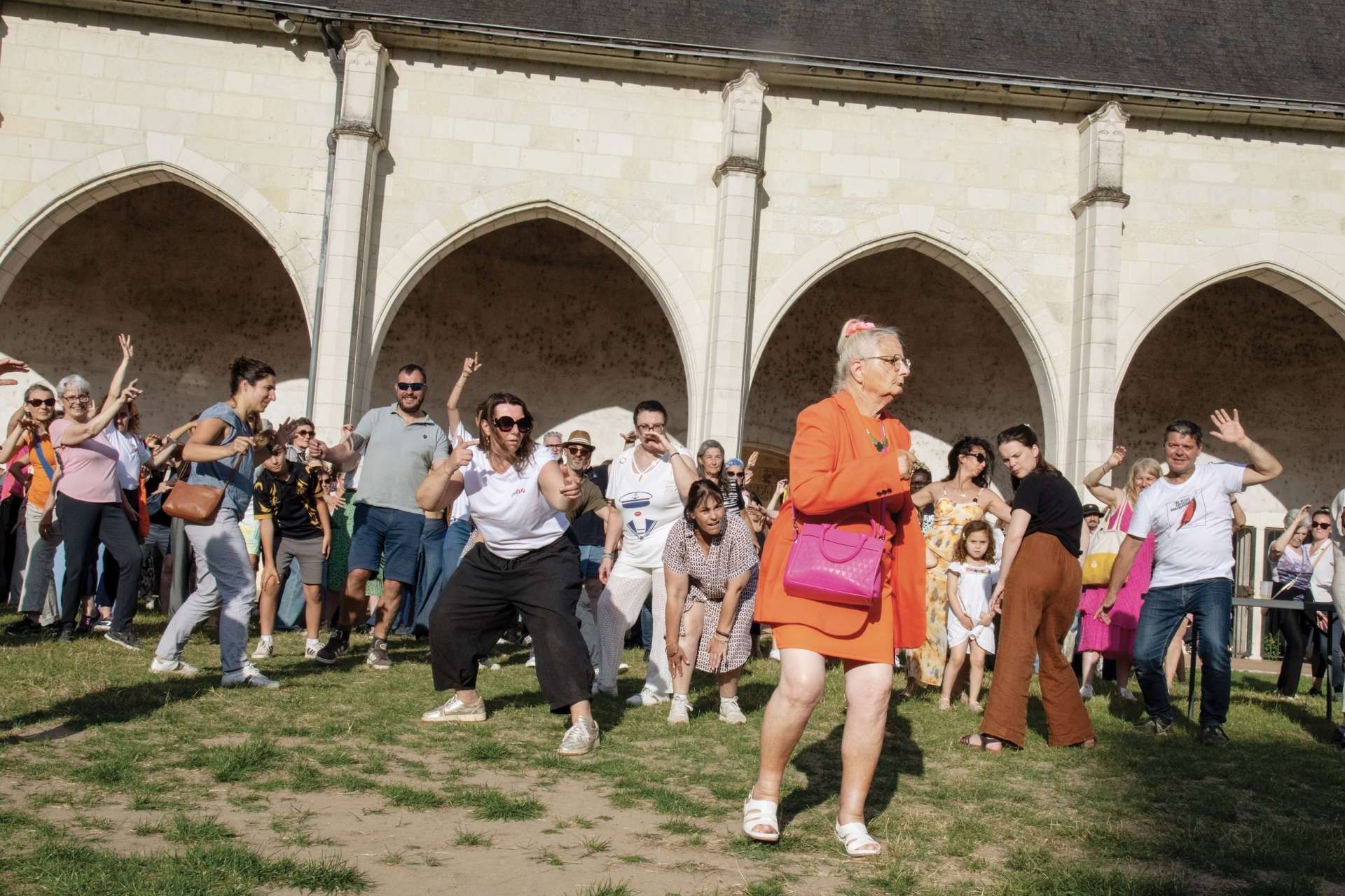 De nombreuses personnes de tous les âges dansent sur la pelouse du Campo Santo à Orléans. Au premier plan, une femme âgée avec une robe orange. 