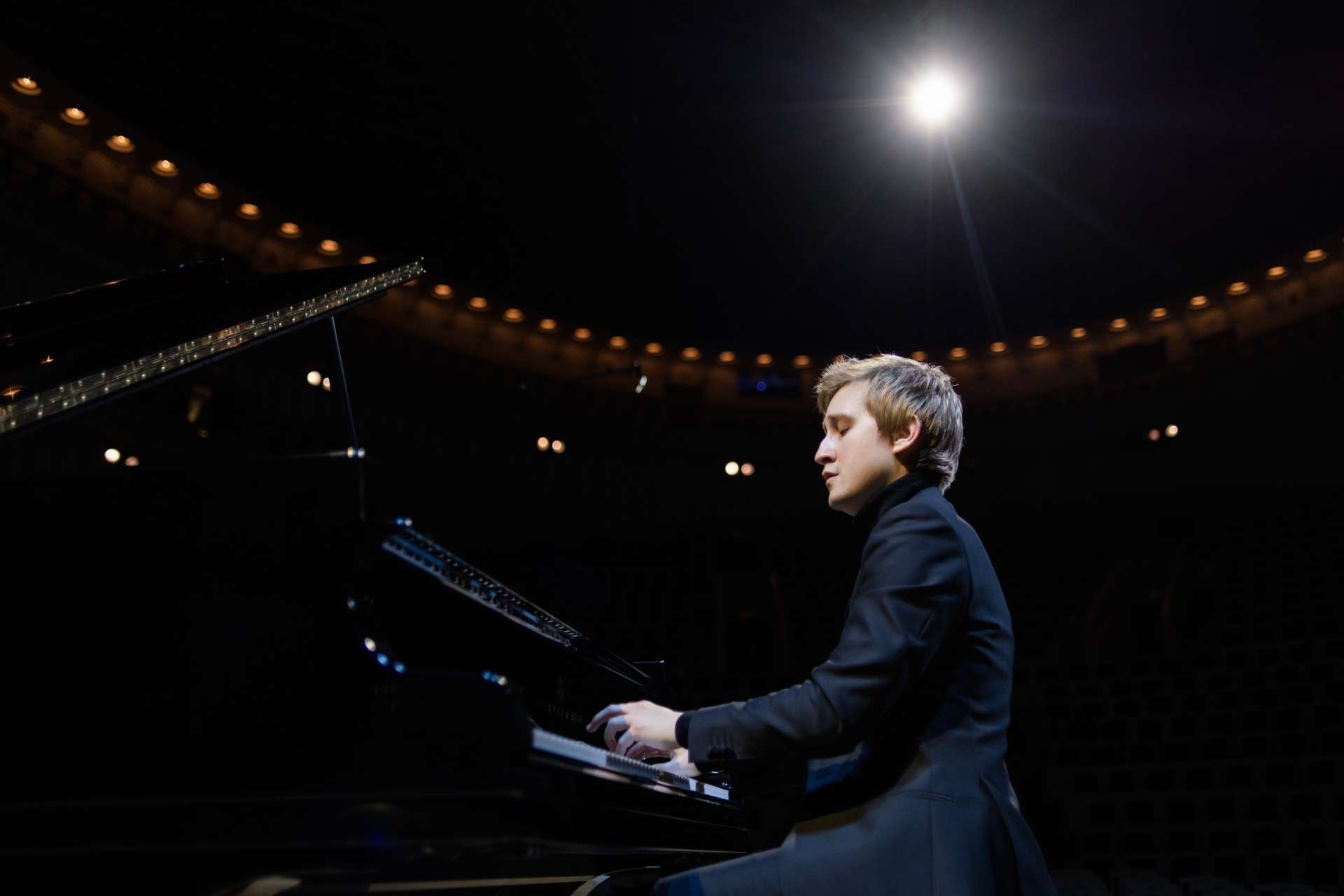 Portrait de Dmitry Masleev jouant du piano avec l'éclairage d'un concert. 