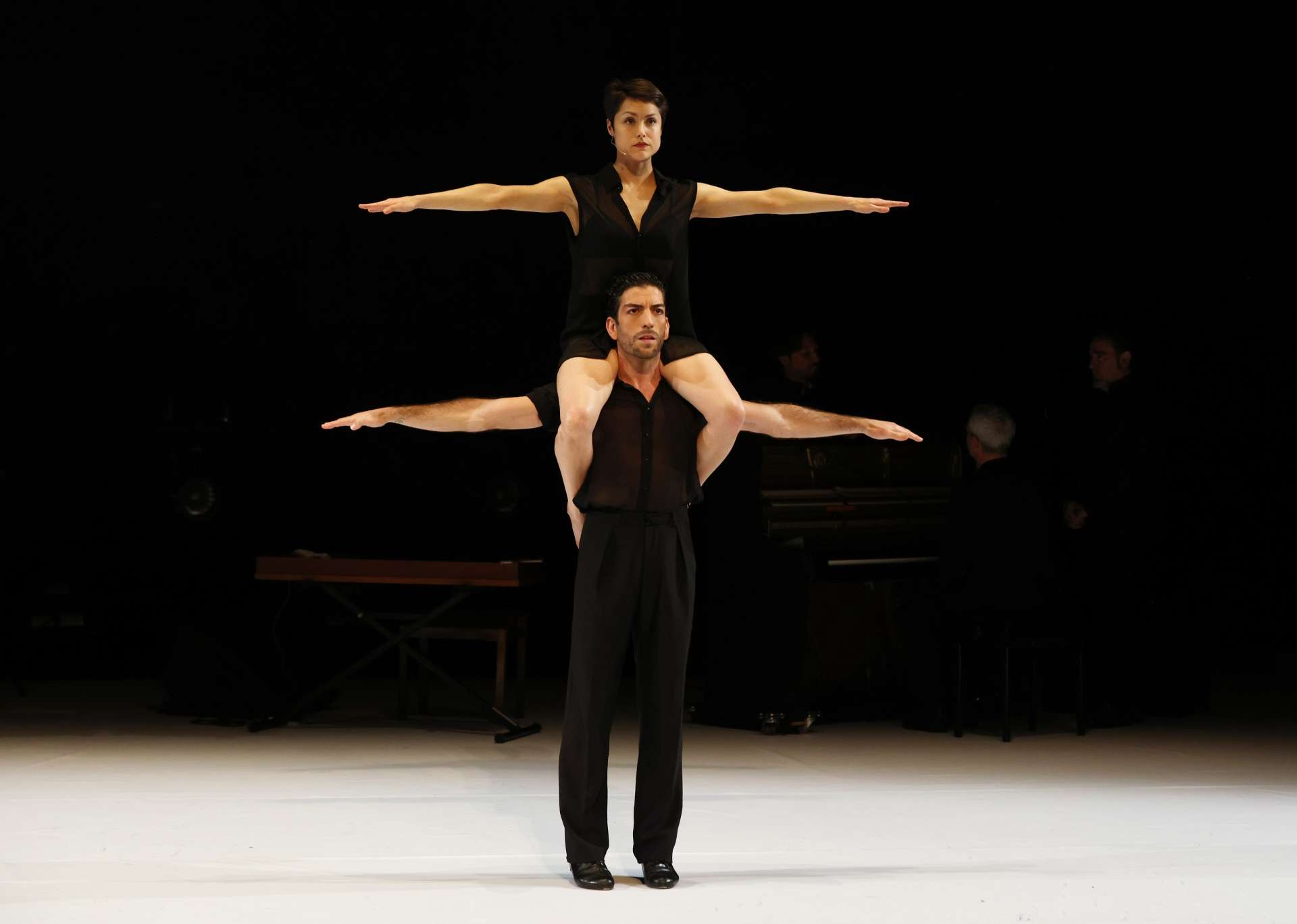 Debout les bras ouverts et tendus sur le côté, le danseur David Coria porte sur ses épaules la danseuse Jann Gallois qui réalise la même figure avec ses bras. 