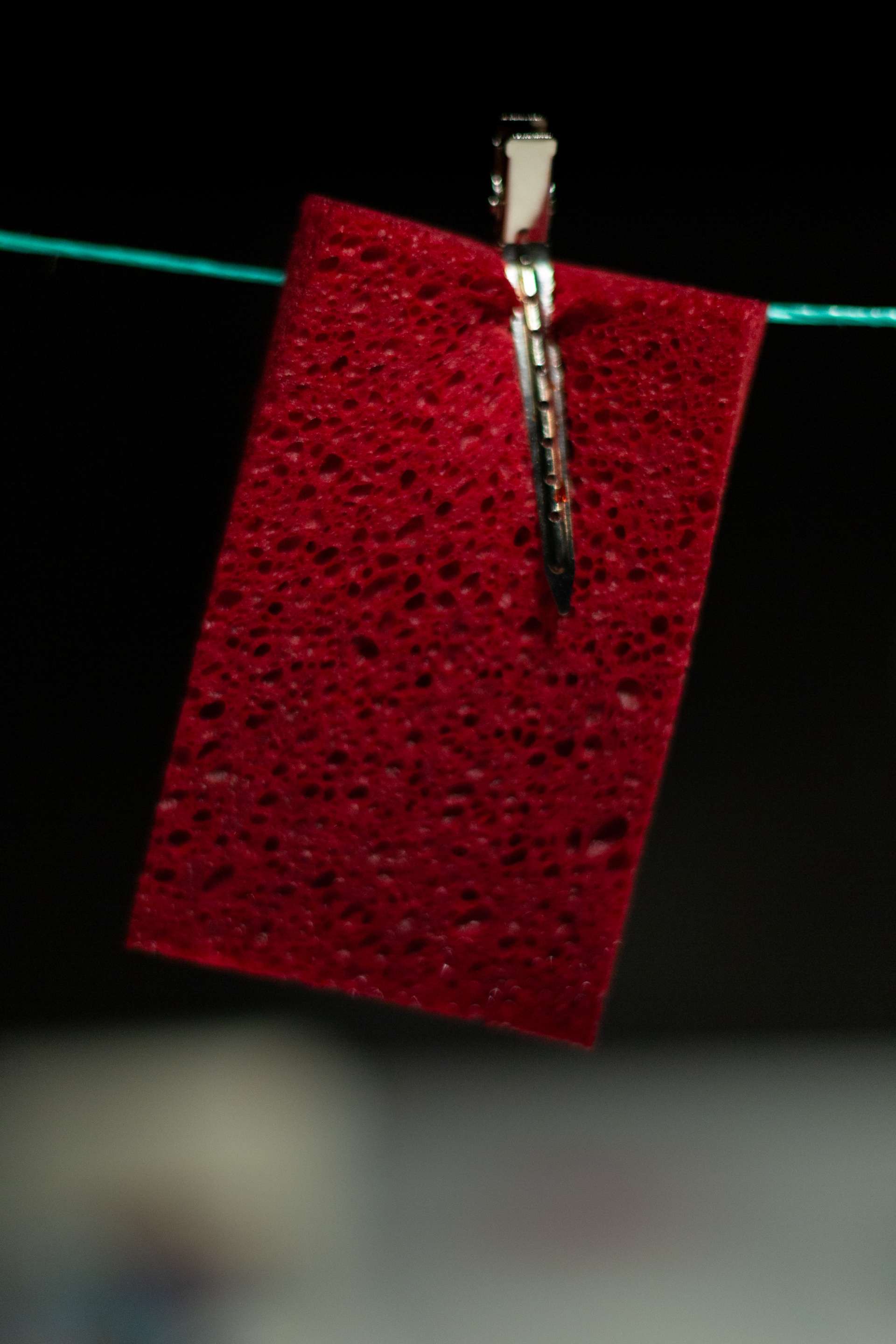 Une éponge rouge suspendue à un fil vert par une pince métallique.