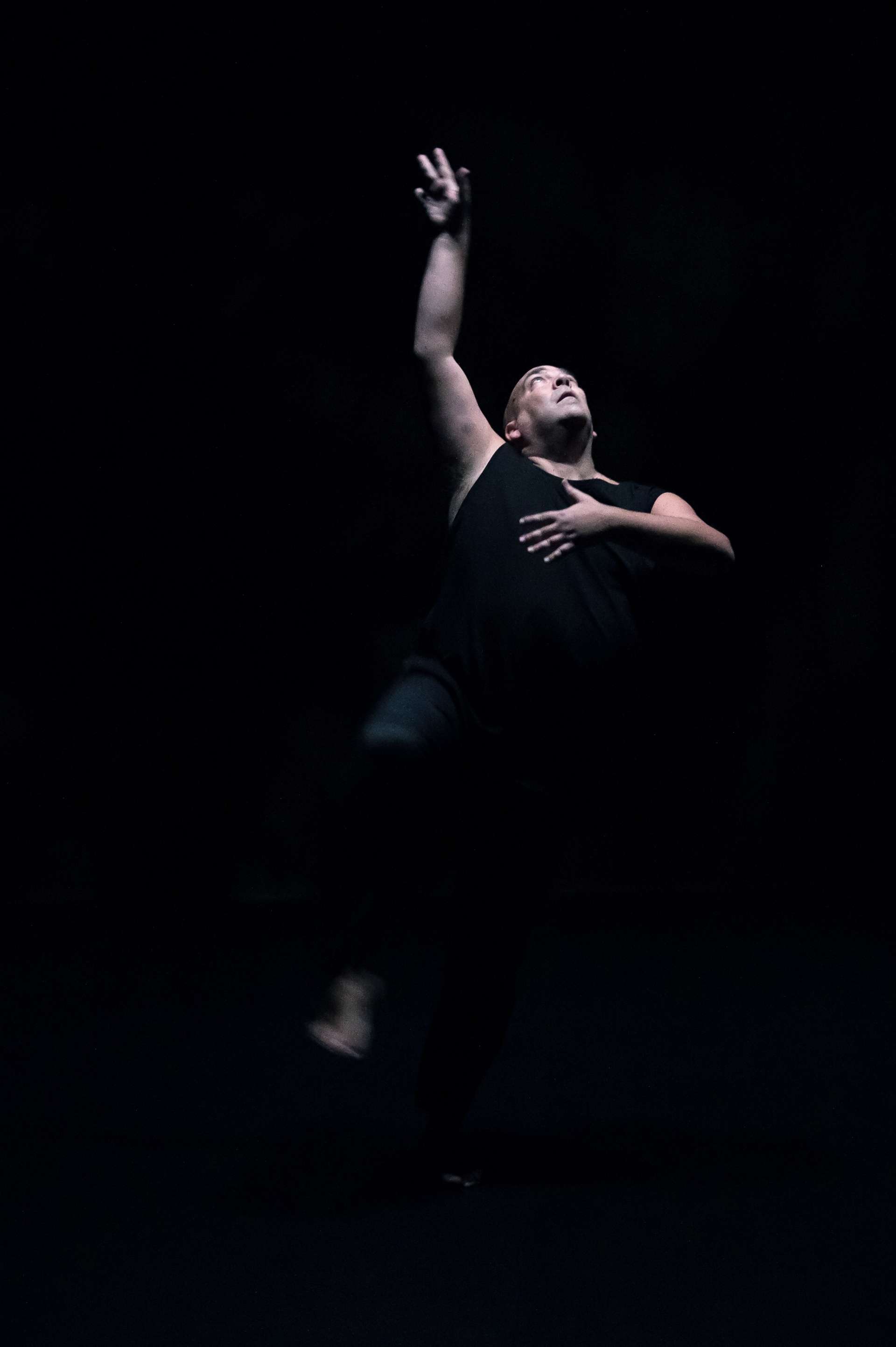 Fond noir et robe noire pour Thomas Lebrun. Il danse, une main en l'air et sa main gauche sur le cœur. 
