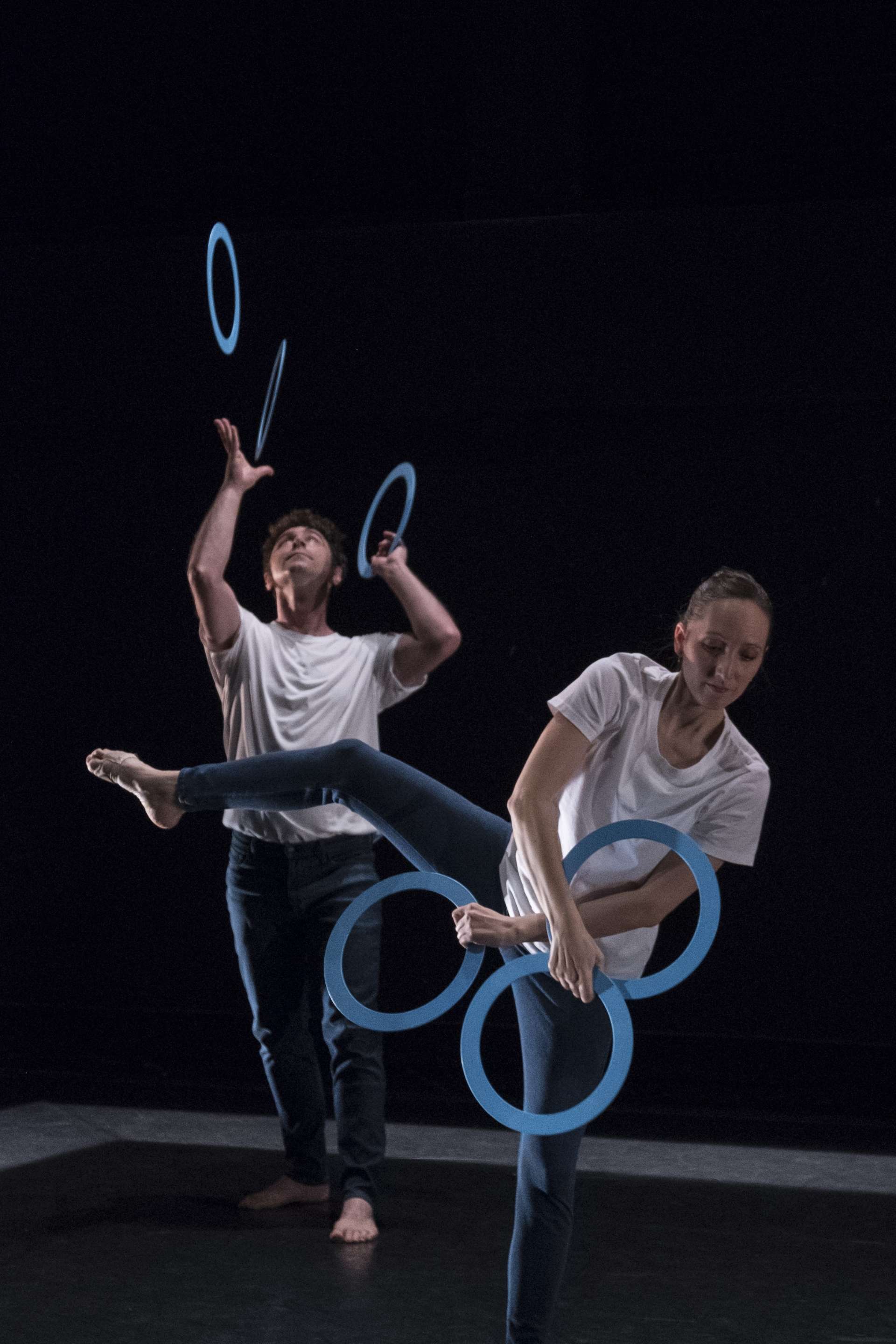Une danseuse et un danseur interprète des mouvements de danse et de jonglage avec les cerceaux bleus. 