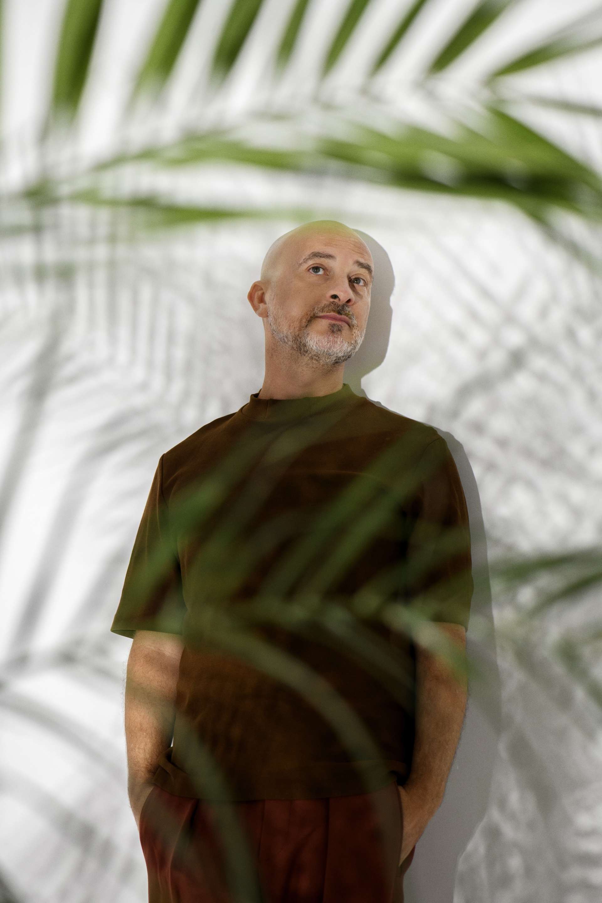 Portrait de Lucas Santtana sur un mur blanc avec des jeux d'ombres autour de la végétation. 
