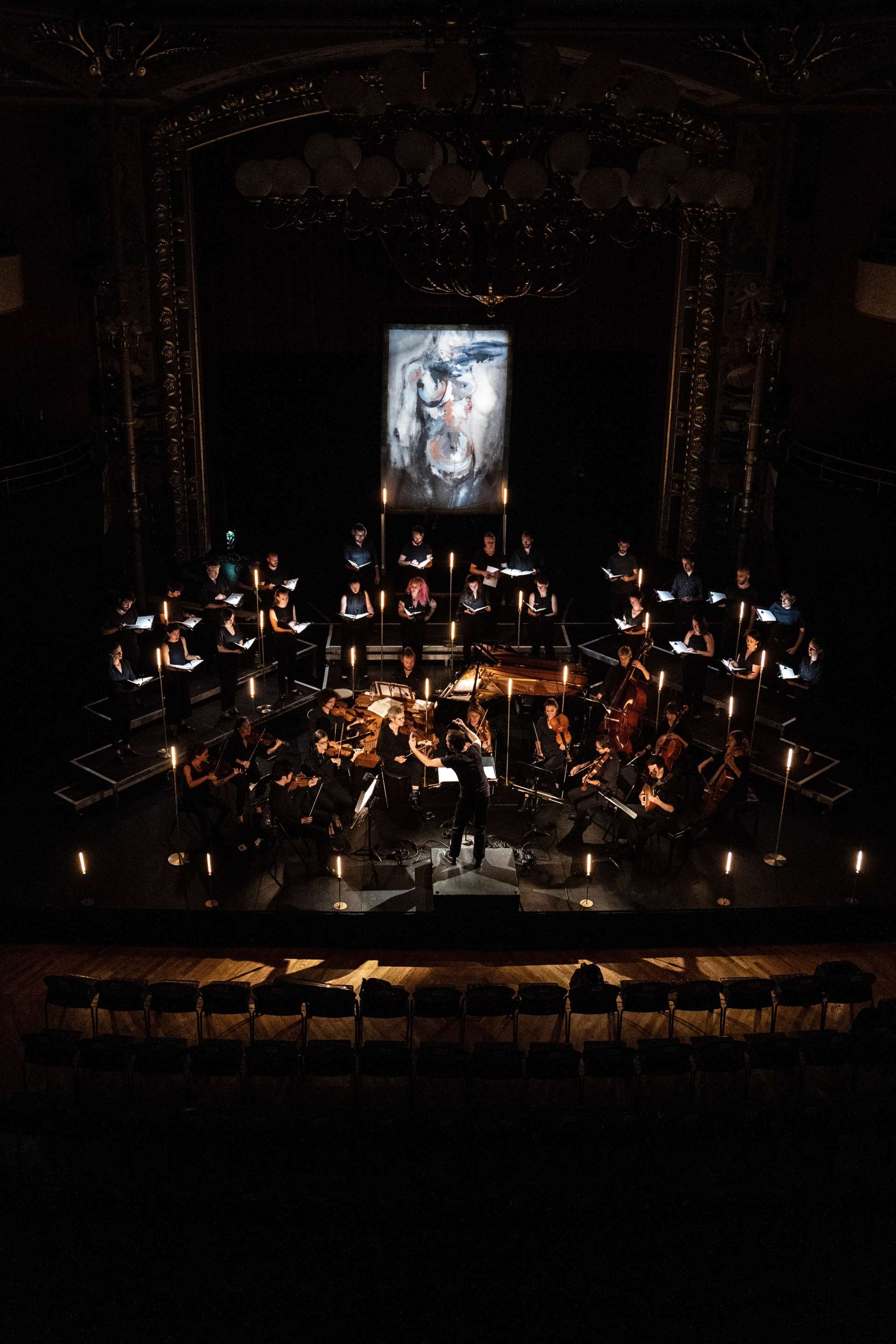 Sur scène, les 46 musiciens et musiciennes sont installés en demi-cercle face au chef d'orchestre Simon-Pierre Bestion. En fond de scène, un grand tableau est présent. 