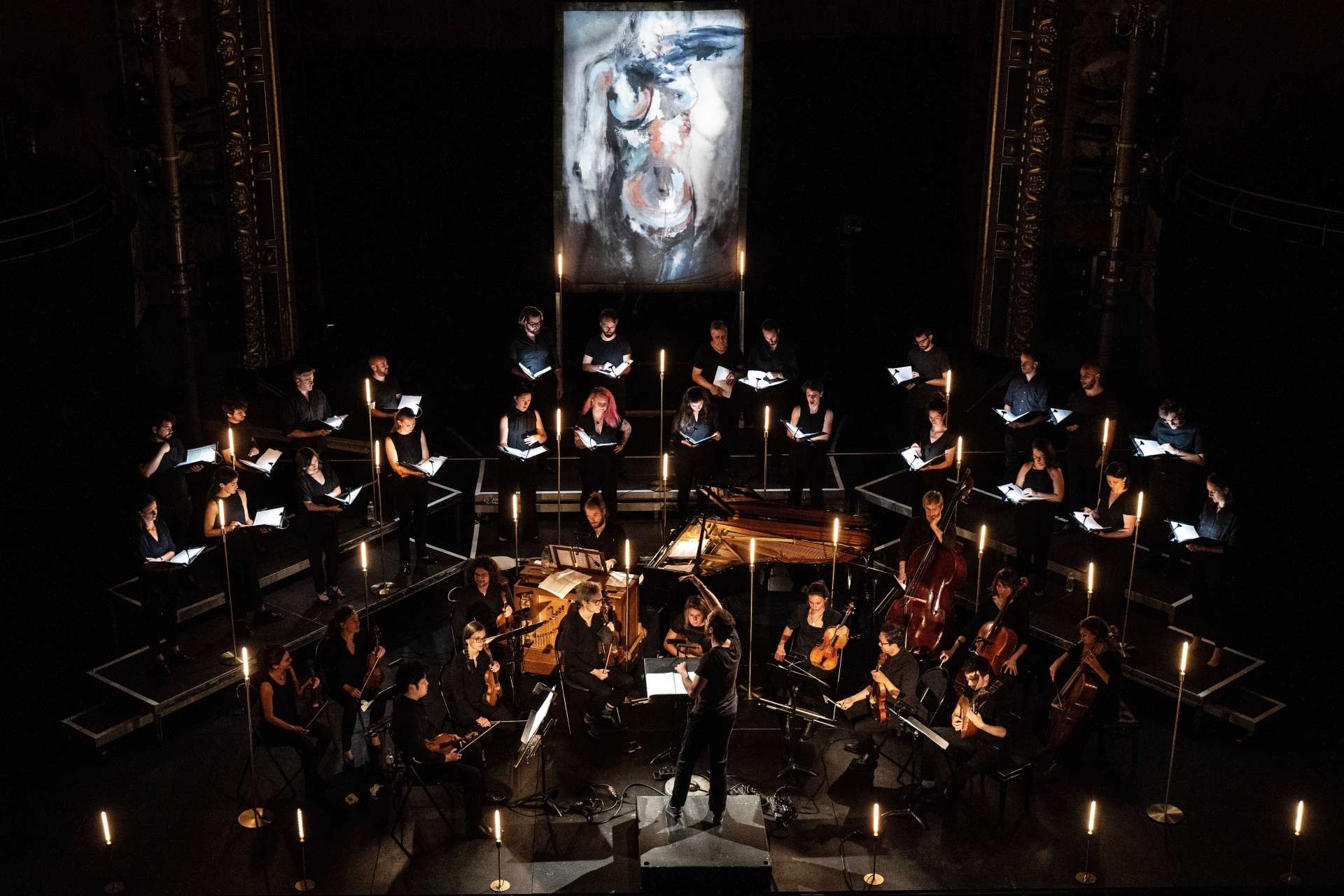 Sur scène, les 46 musiciens et musiciennes sont installés en demi-cercle face au chef d'orchestre Simon-Pierre Bestion. En fond de scène, un grand tableau est présent. 