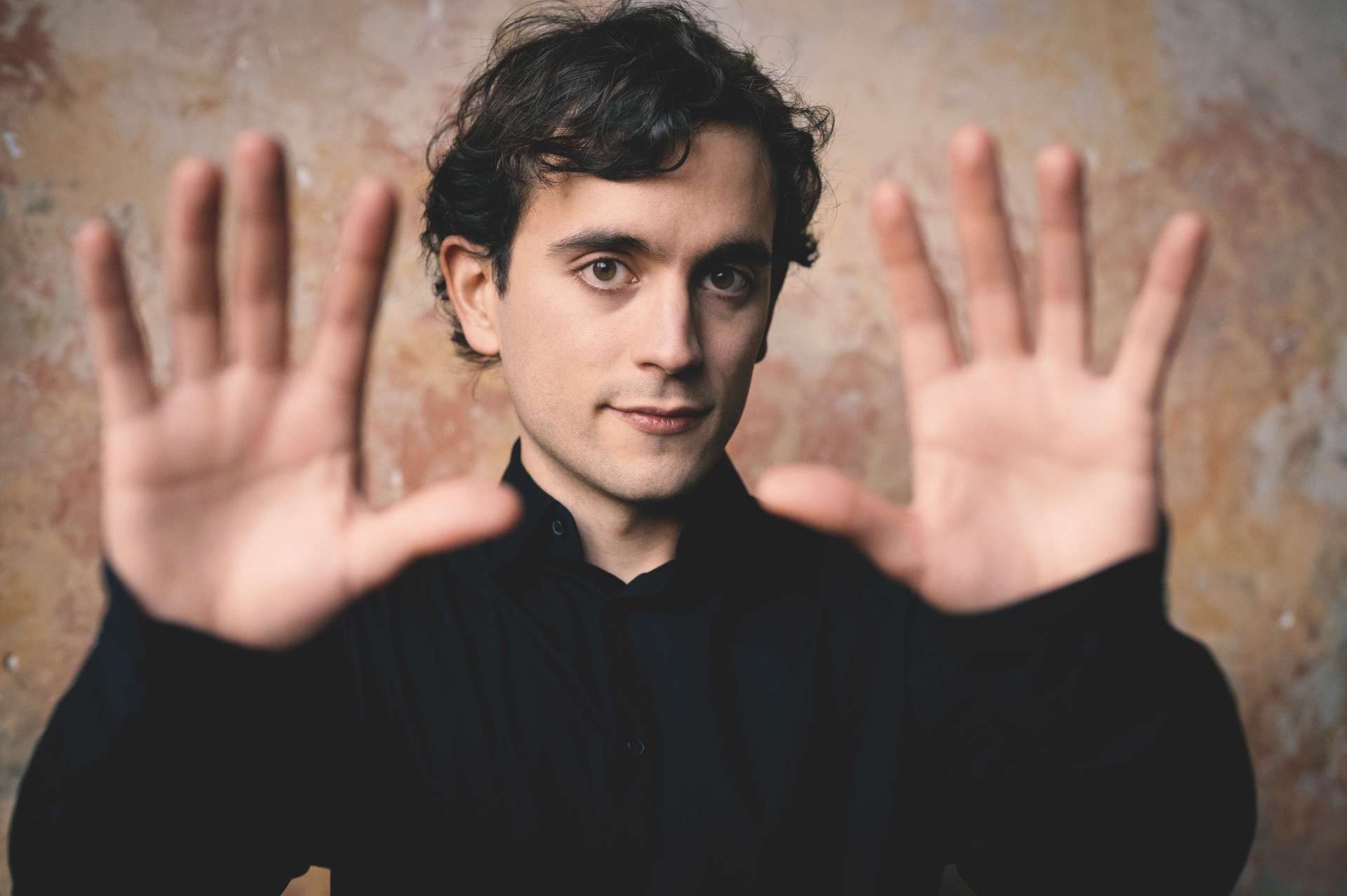 Le pianiste Lorenzo Soulès, face à l'objectif, ses deux mains grandes ouvertes encadrant son visage