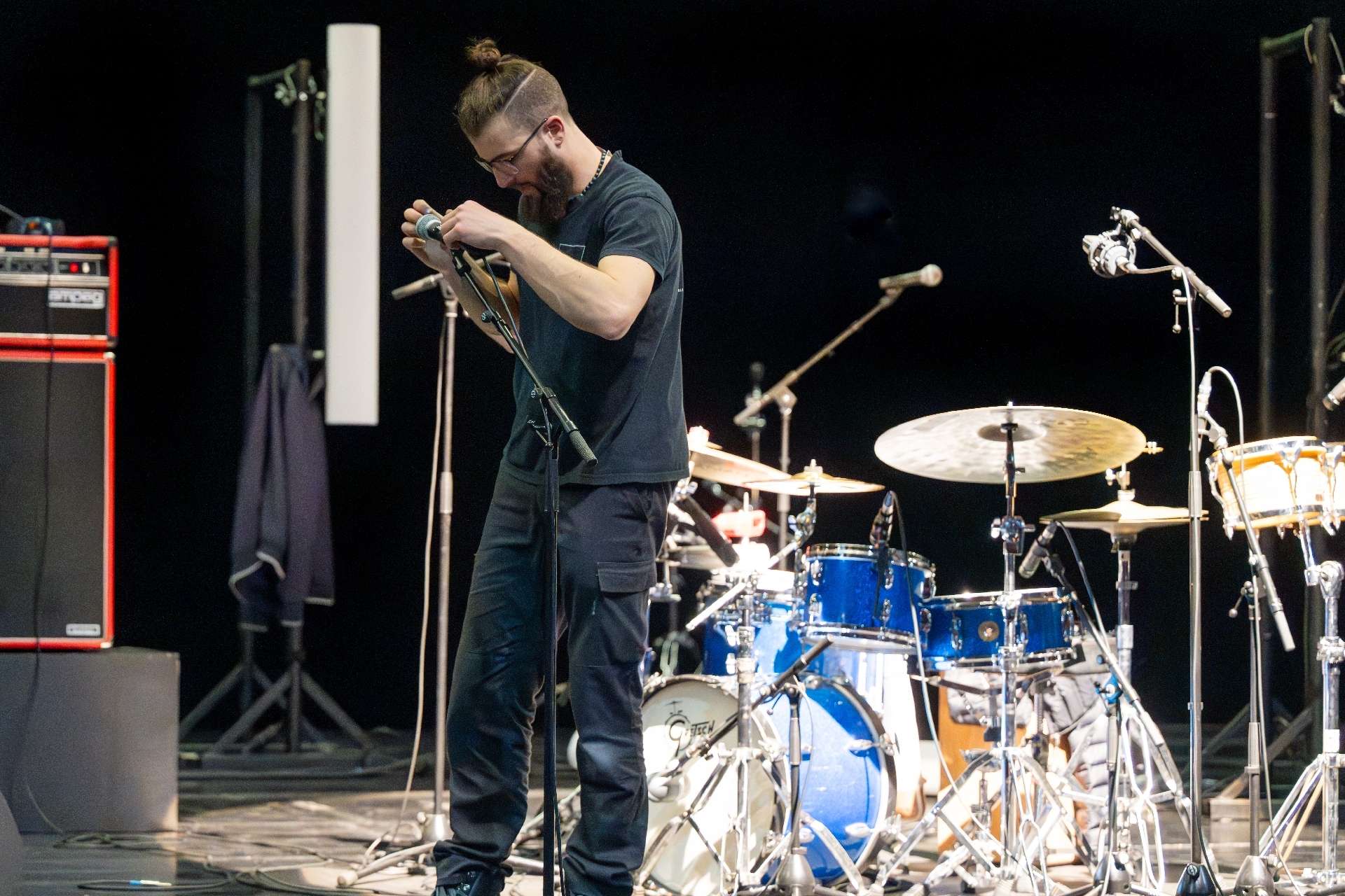 Technicien accrochant un micro sur un pied, des instruments sont sur le plateau derrière lui.