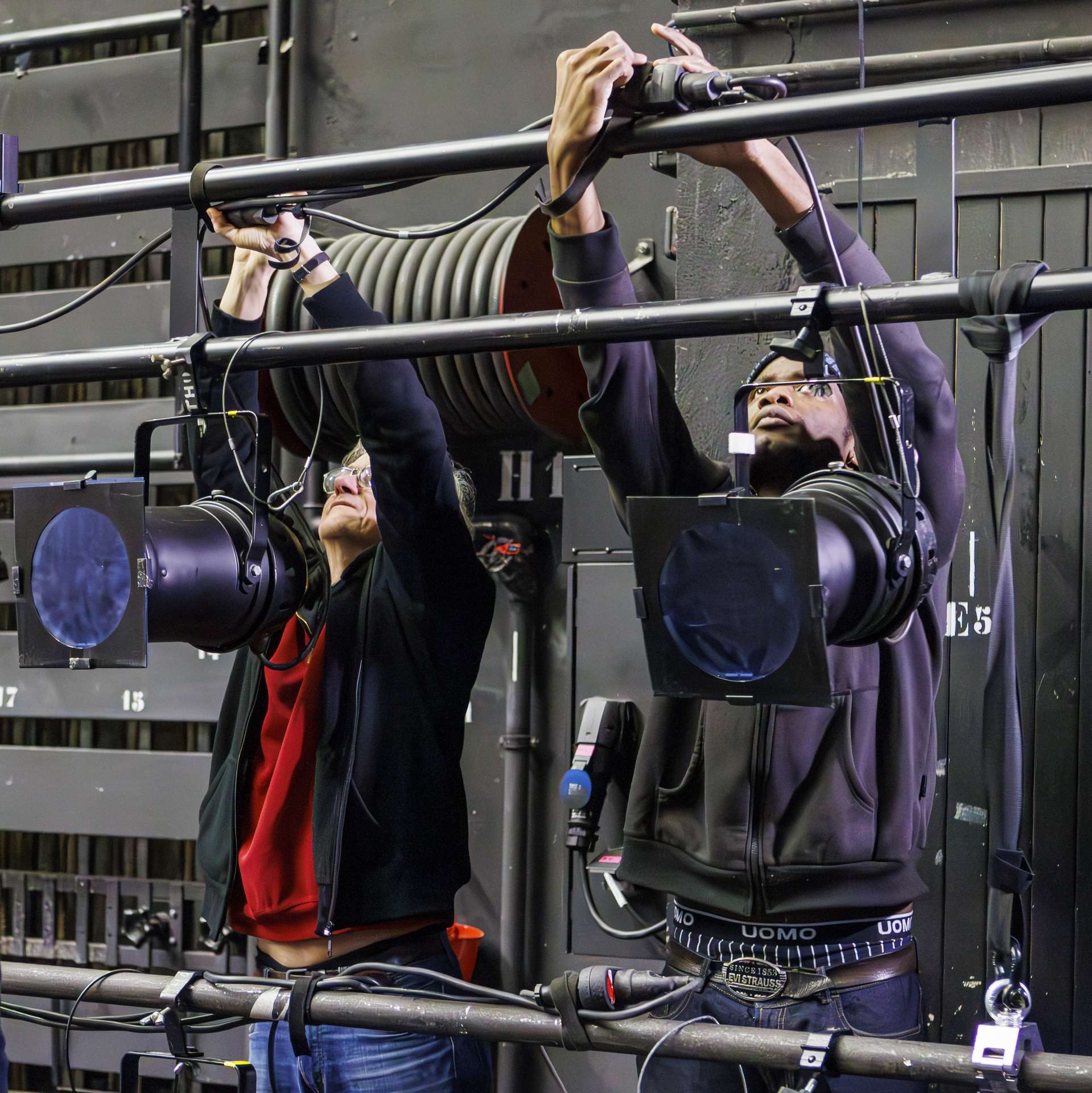 Deux techniciens branchent des projecteurs sur une perche.