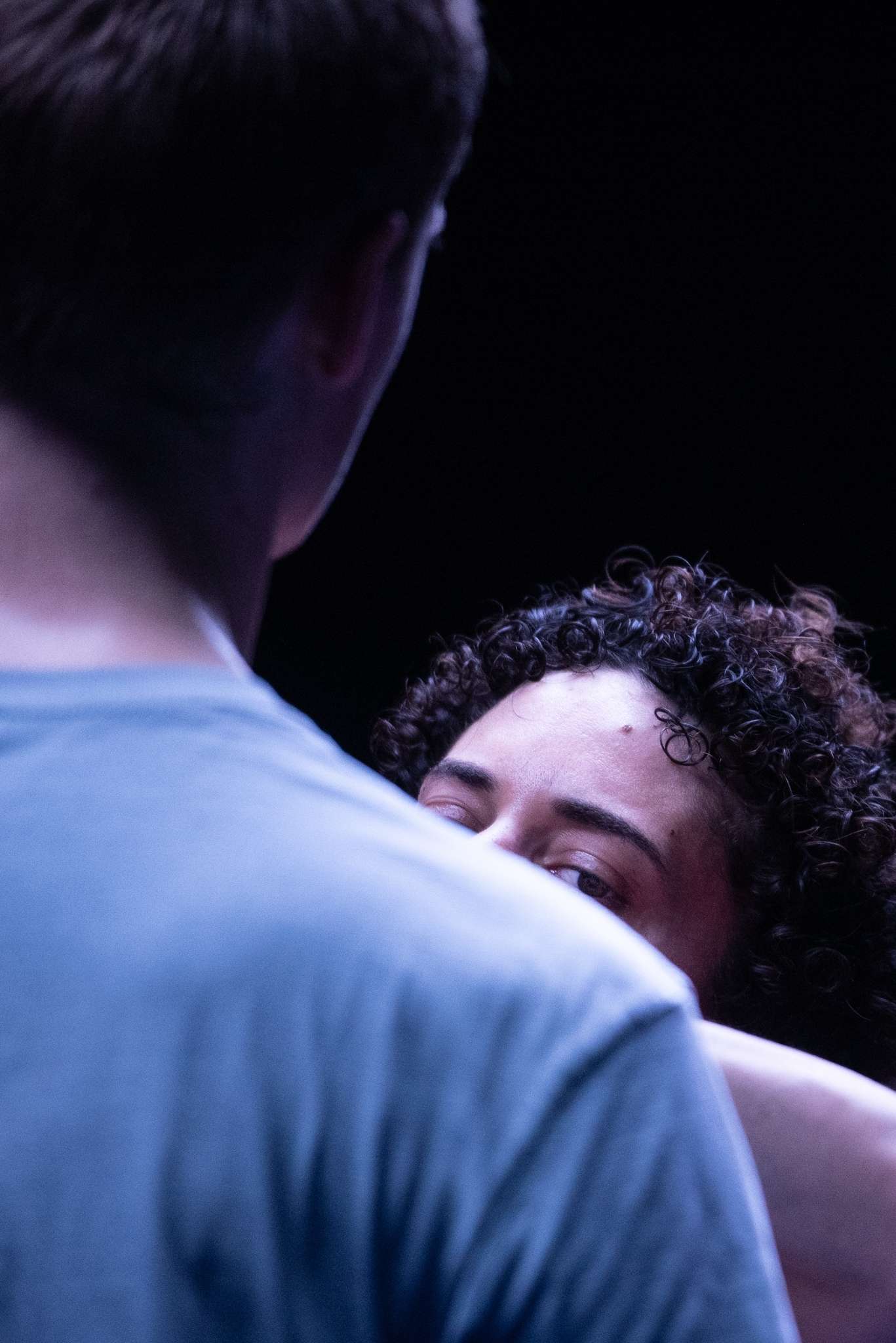 Au premier plan, l'épaule d'un homme et au second plan une femme qui regarde par dessus. 