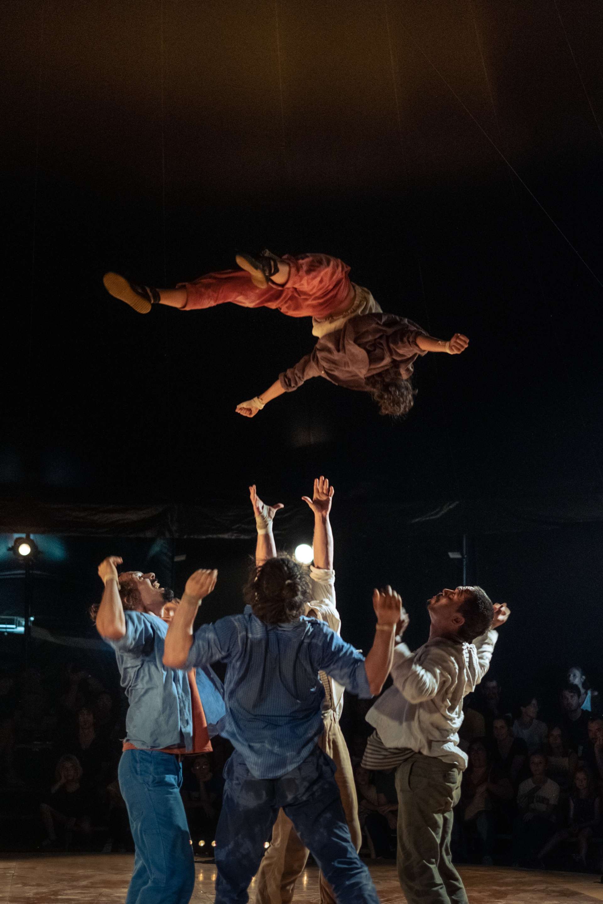 Porté acrobatique avec l'un des interprètes qui volent à plat dos. En dessous, les autres acrobates se tiennent prêts, mains levées, à le rattraper. 