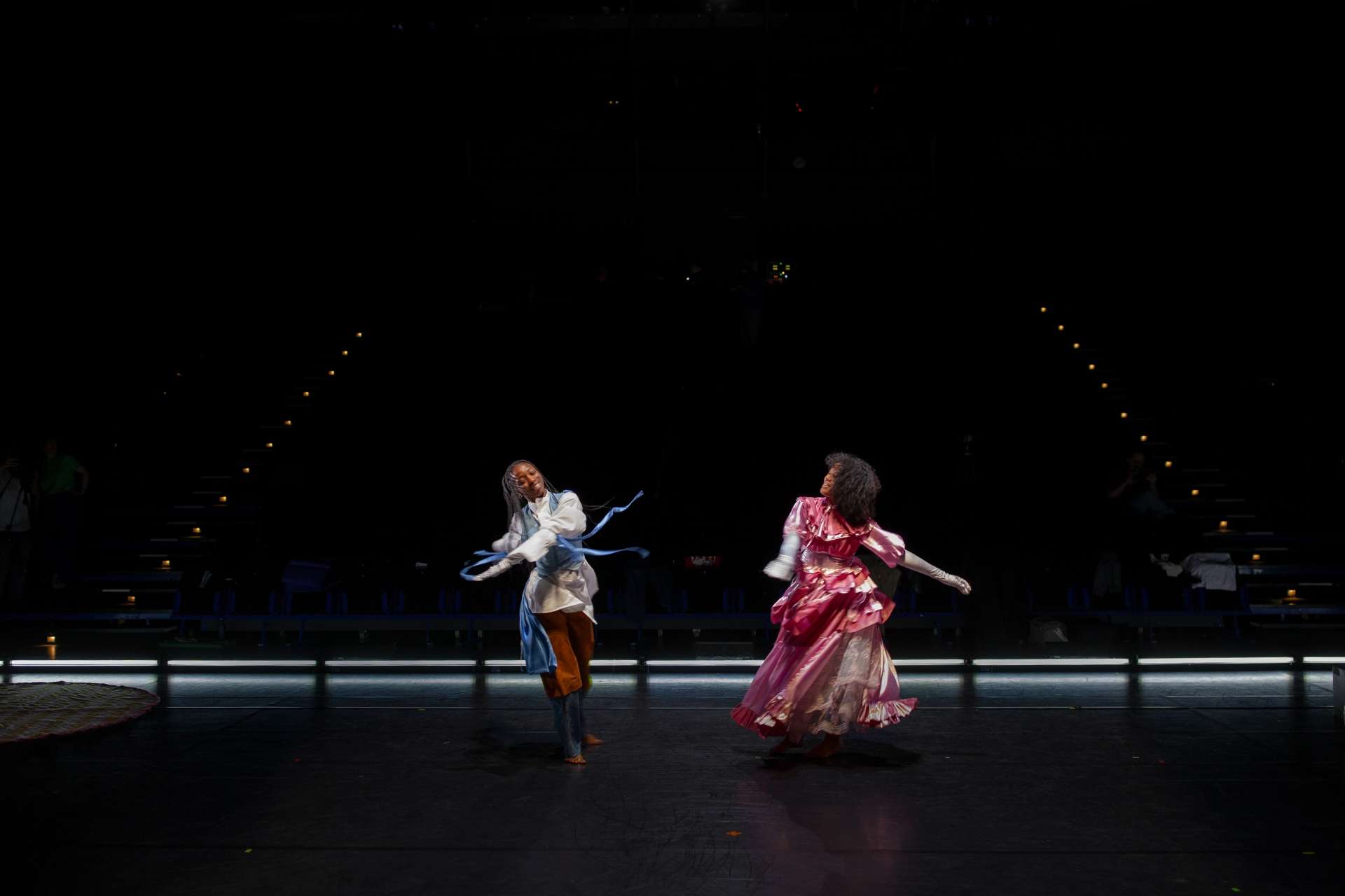 Deux interprètes féminines dansent avec des costumes colorés, tenue blanche et bleue pour l'une et robe rose pour l'autre. 