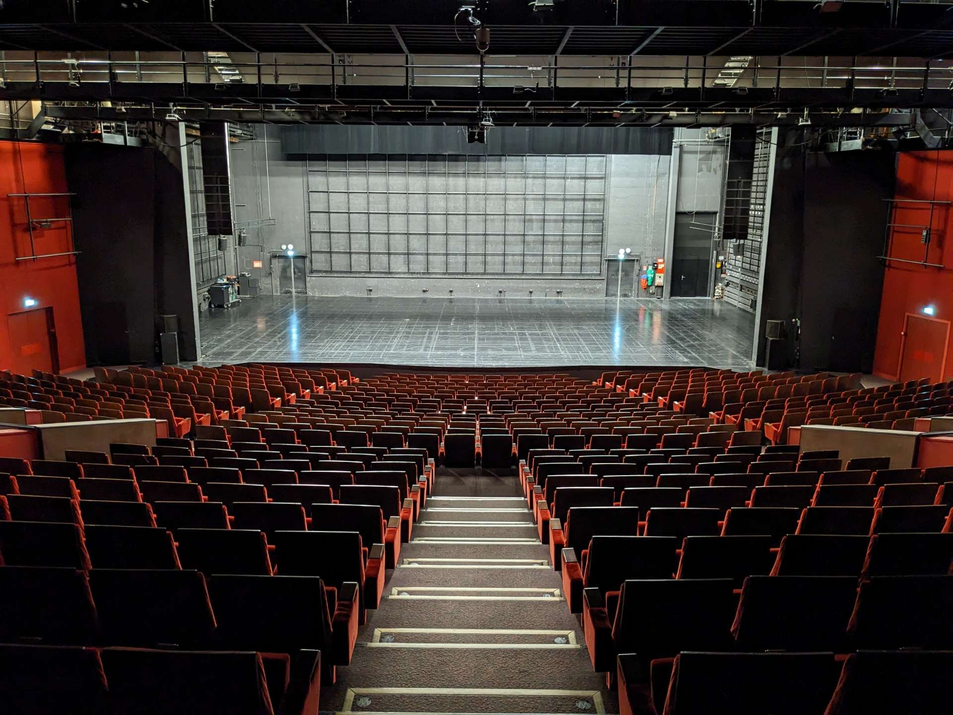 Vue de la salle Touchard côté salle avec au premier plan les fauteuils rouges et au second le plateau. 