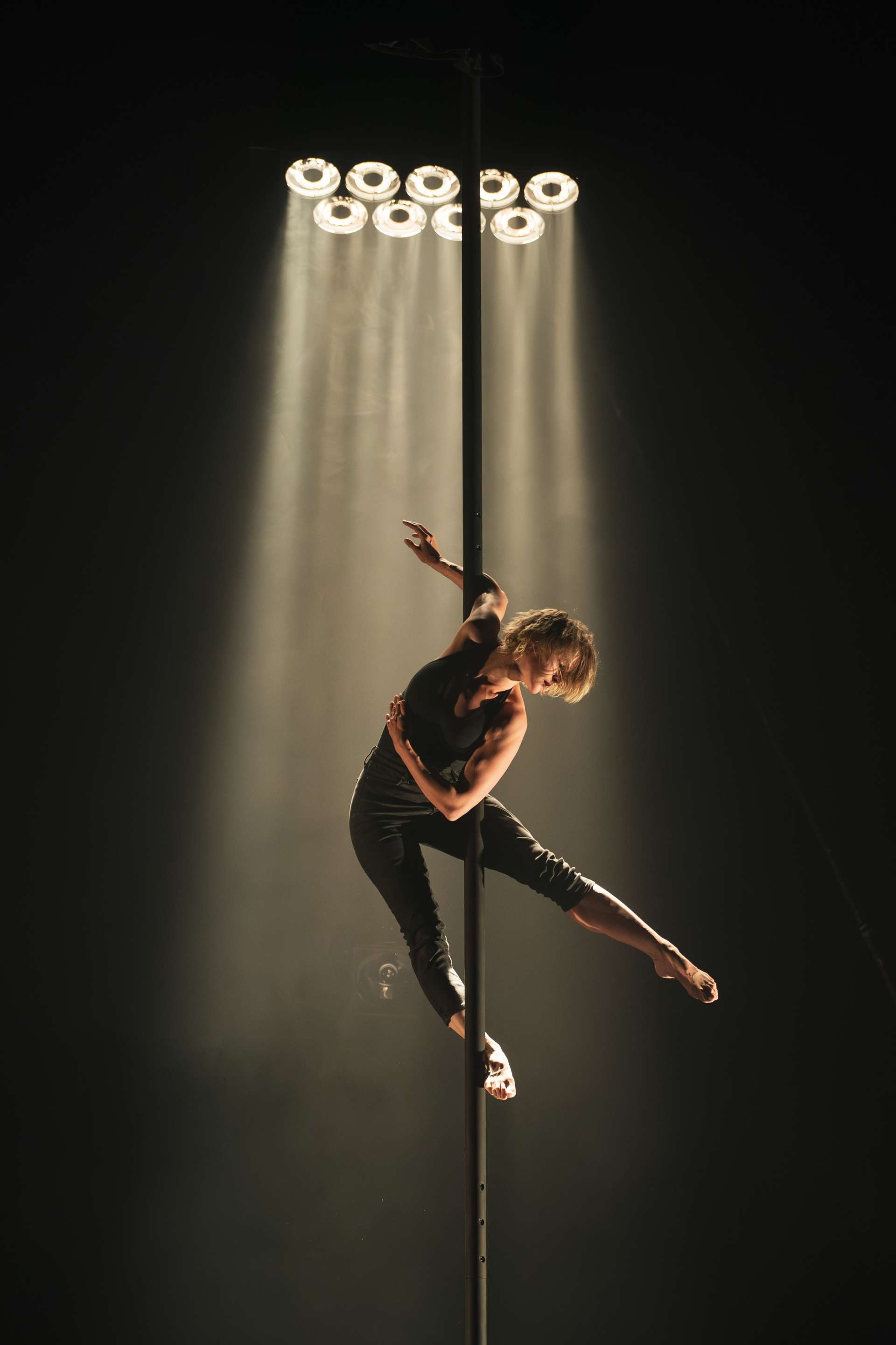 Tel un ange suspendu, une acrobate se tient sur un mat chinois. est accrochée en l'air. La lumière luit sur elle. 