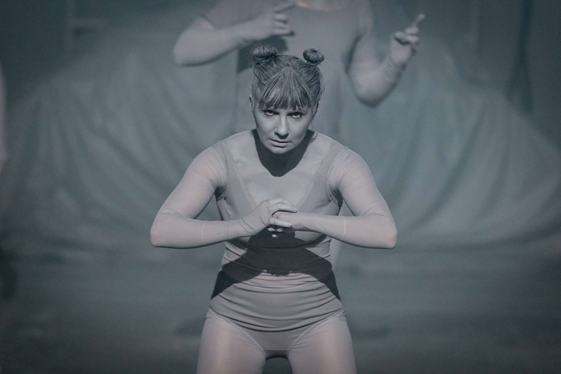 Fond gris, une femme en maillot de bain est au centre de la photo et semble être en position de haka. 