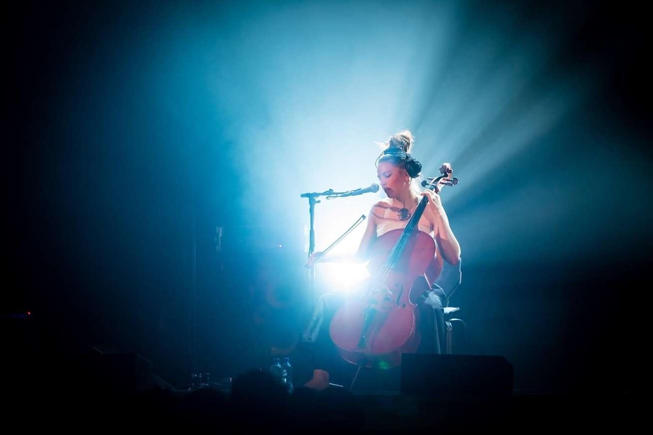 Photo de Lana Kostic qui joue du violoncelle sur scène, éclairée par un projecteur.